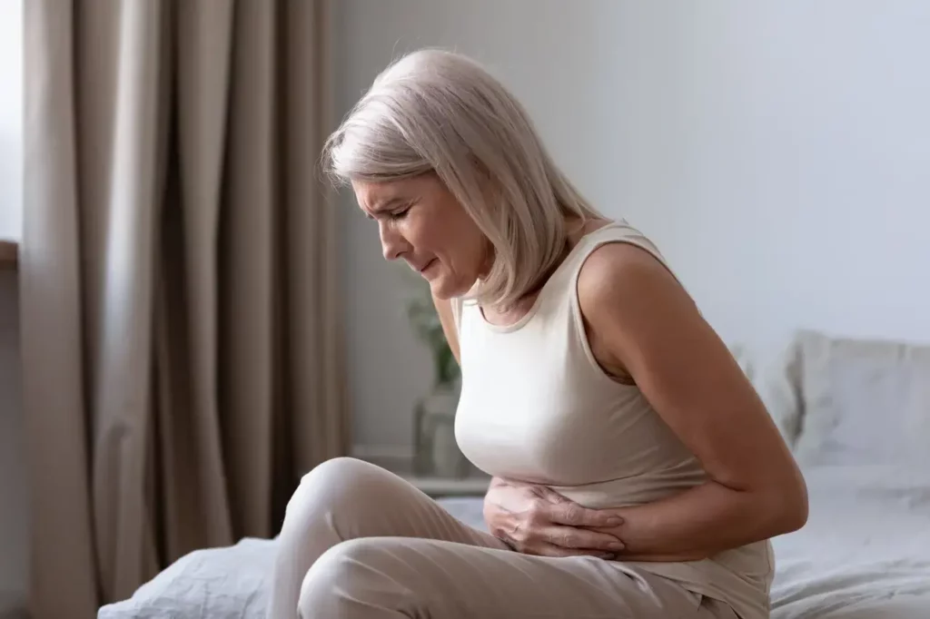 A woman in her late 50s holds her stomach in pain due to a stomach ulcer