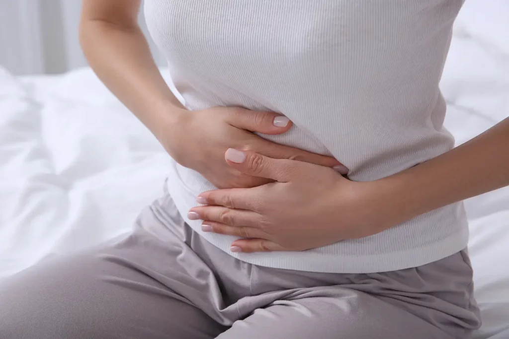 A woman sat on her bed holds her tummy in discomfort caused by a UTI