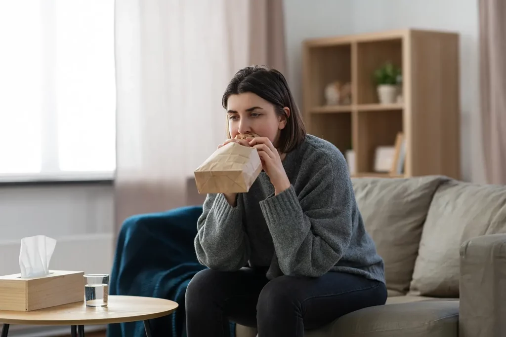 A woman breathes into a paper bag to regulate her breathing due to a panic attack.