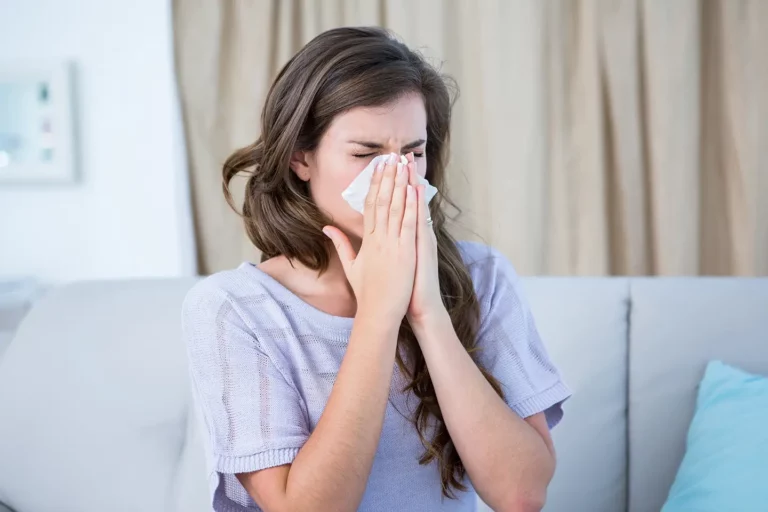 A woman blows her nose into a tissue because her nose is blocked