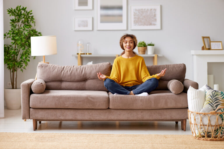 A teenage girl sits on the sofa, jokingly pretending to meditate.