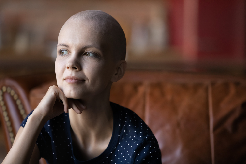 A bald woman with cancer sits in deep thought, she looks positive about her future.