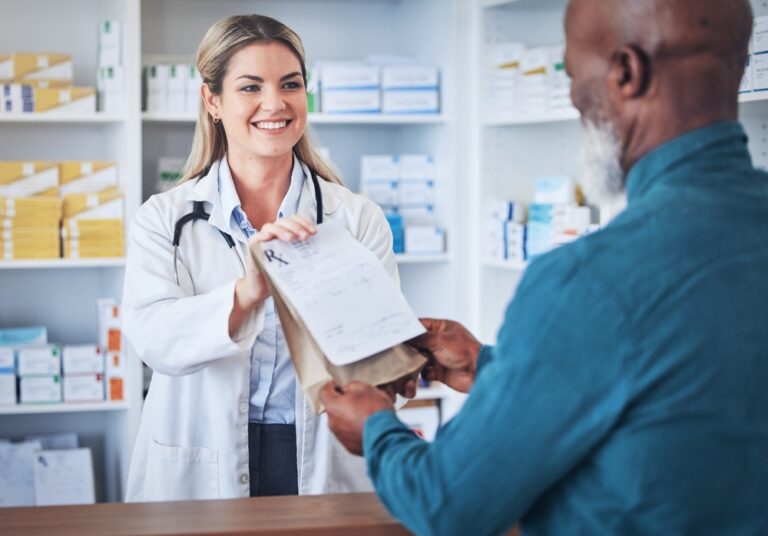 A man collects his prescription from a smiling pharmacist behind the counter