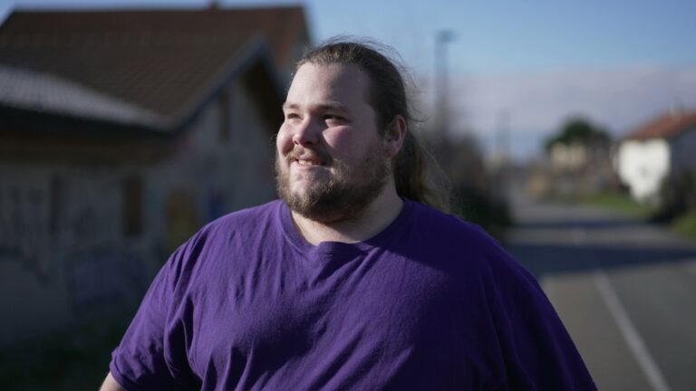 An overweight man smiles as he takes a walk after exercising on his stationary bike.