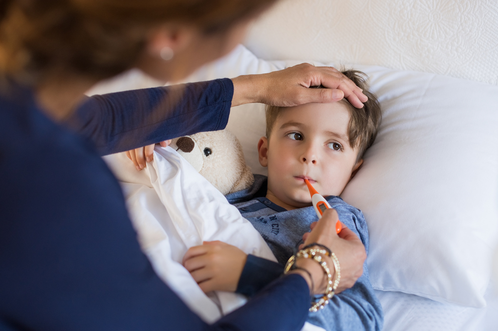 A young boy is in bed with a sinus infection, while his mother takes his temperature
