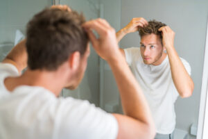 A man checks his hair in the mirror to check his hair growth after using rosemary oil.